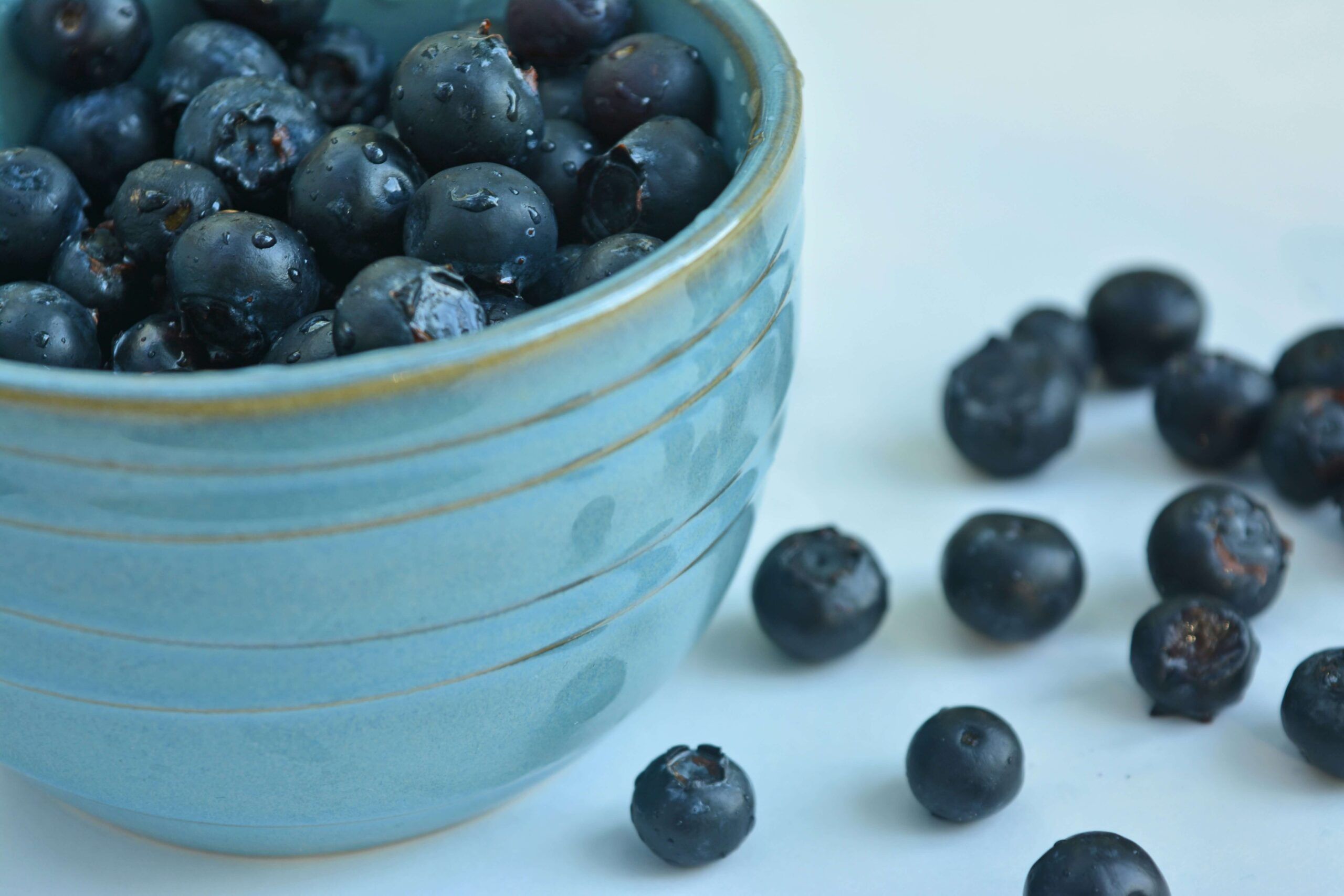 A blue bowl holding blueberries on a table with blueberries scattered. Working with a dietitian in Raleigh, NC can help with eating disorders, chronic conditions & more. Call now to begin your healing journey.