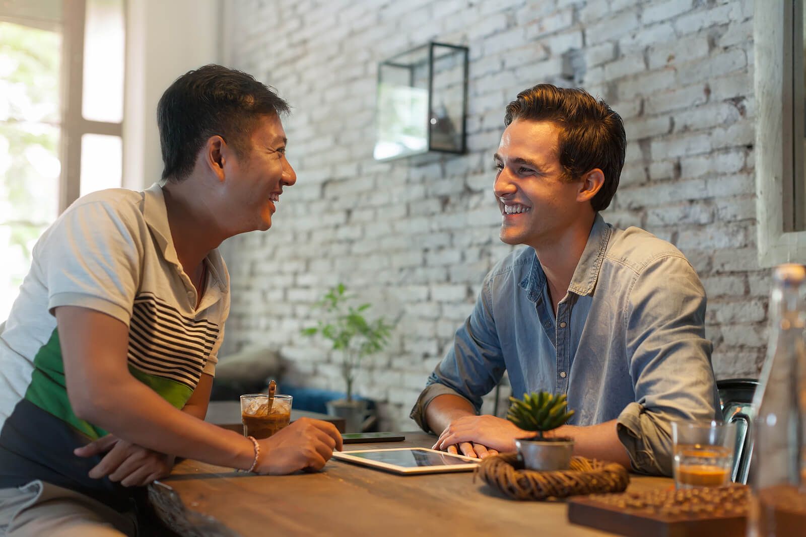 Two men smiling at each other while sitting down at a cafe. Our nutrition therapy can help with chronic conditions, disordered eating & body image. Start working with a dietitian in Raleigh, NC today.