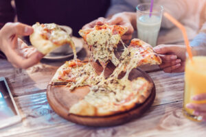 A pizza sitting on a table with different hands reaching for a slice. Nutrition therapy in Asheville, NC can help with disordered eating patterns. Call today to get started!