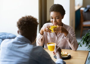 Two individuals sitting down at a coffee shop drinking coffee from yellow mugs. A nutritionist in Raleigh, NC can help you break up with diet culture. Get started with eating disorder therapy today.