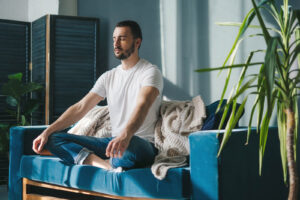 A man sitting in a meditated pose on a blue couch. Our nutrition therapy in Raleigh, NC can address chronic dieting & disordered eating. Call today to get started.