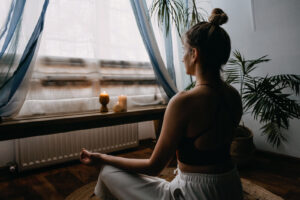 An individual sitting in a meditative pose in front of a window. Nutritional therapy in Cary, NC can help enhance your self-care journey. To learn more, read our blog here!