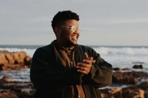 A man smiling while clasping his hands together & standing in front of an ocean view. If you want to build your relationship with food in a safe & supportive environment, reach out to begin nutrition therapy in Raleigh, NC. Contact us today to learn more. 