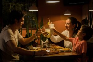 A family of three eating together at the dinner table & cheering their glasses together. Nutrition therapy in Raleigh, NC can help with disordered eating, diabetes management & more. Call today to get started with our dietitians. 